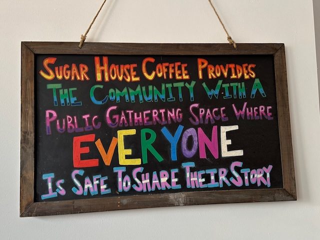 Sign that says SUGAR HOUSE COFFEE PROVIDES THE COMMUNITY WITH A PUBLIC GATHERING SPACE WHERE EVERYONE Is SAFE TO SHARE THEIR STORY