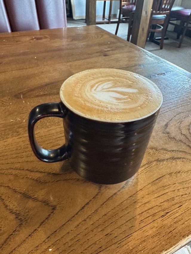Black ceramic mug with latte art sitting on the table.
